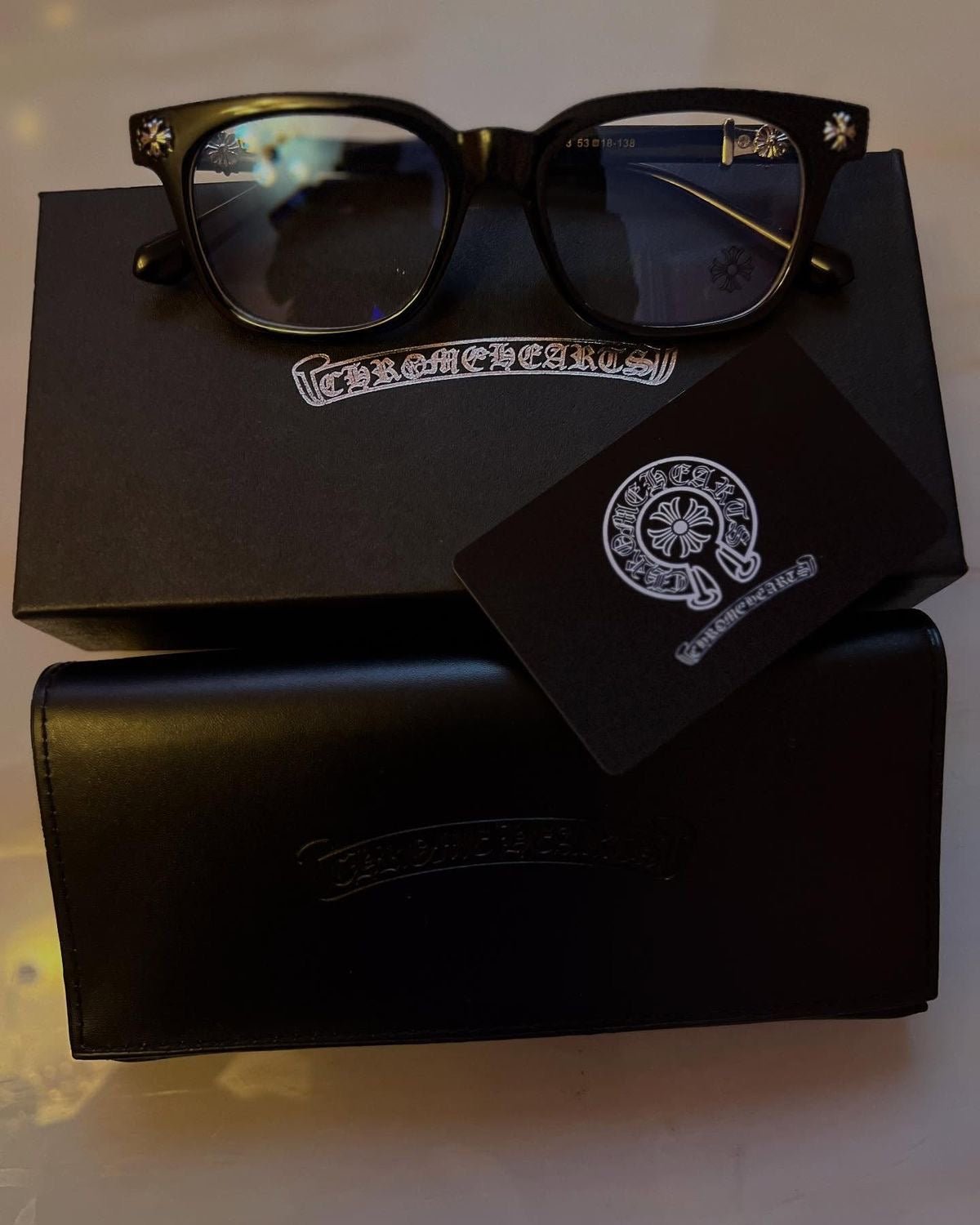 Black sunglasses with a case and card on a black box with branding.