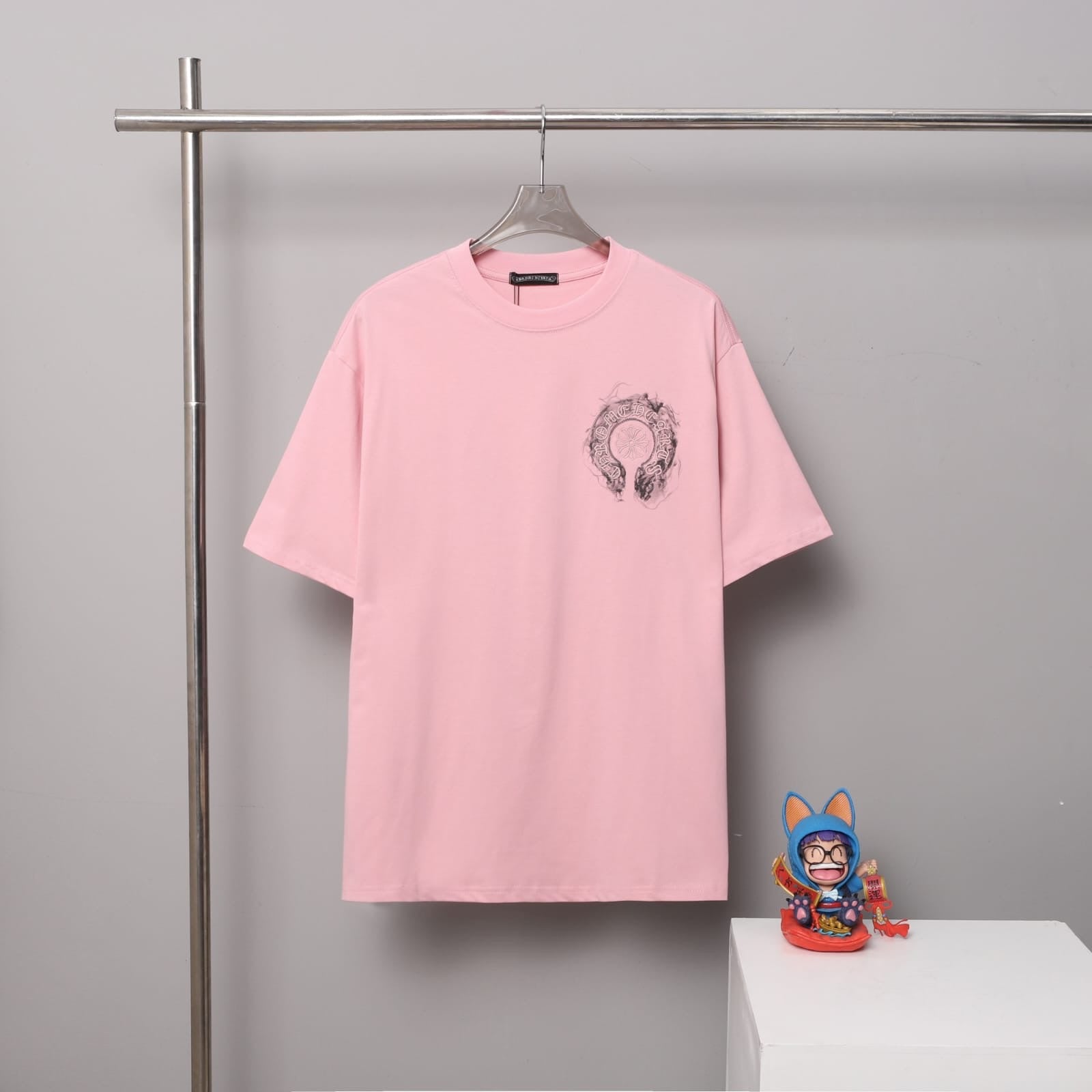 Pink t-shirt with a graphic design on a hanger against a gray background.