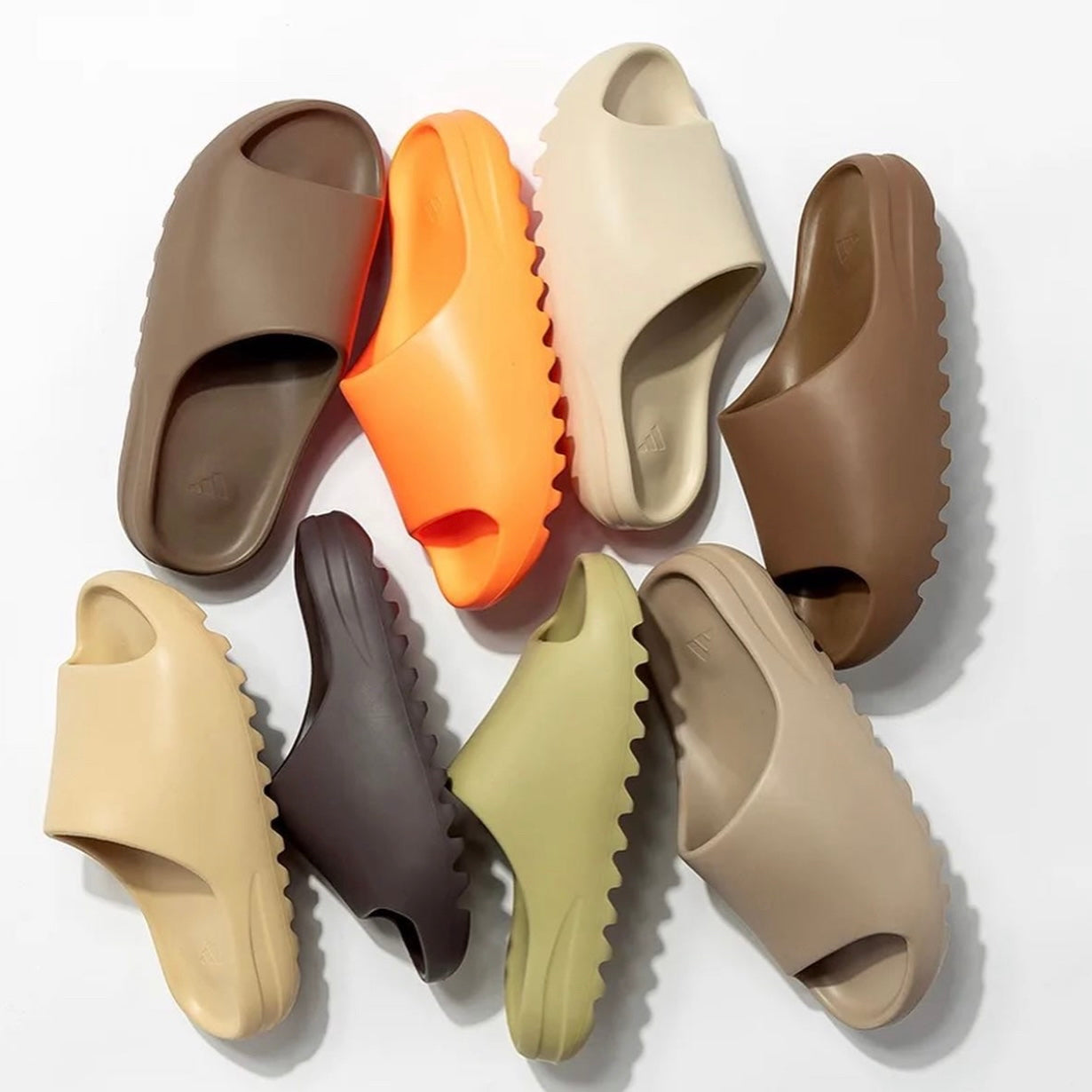 A collection of Adidas Yeezy slides in various colors including black, brown, beige, white, and orange.