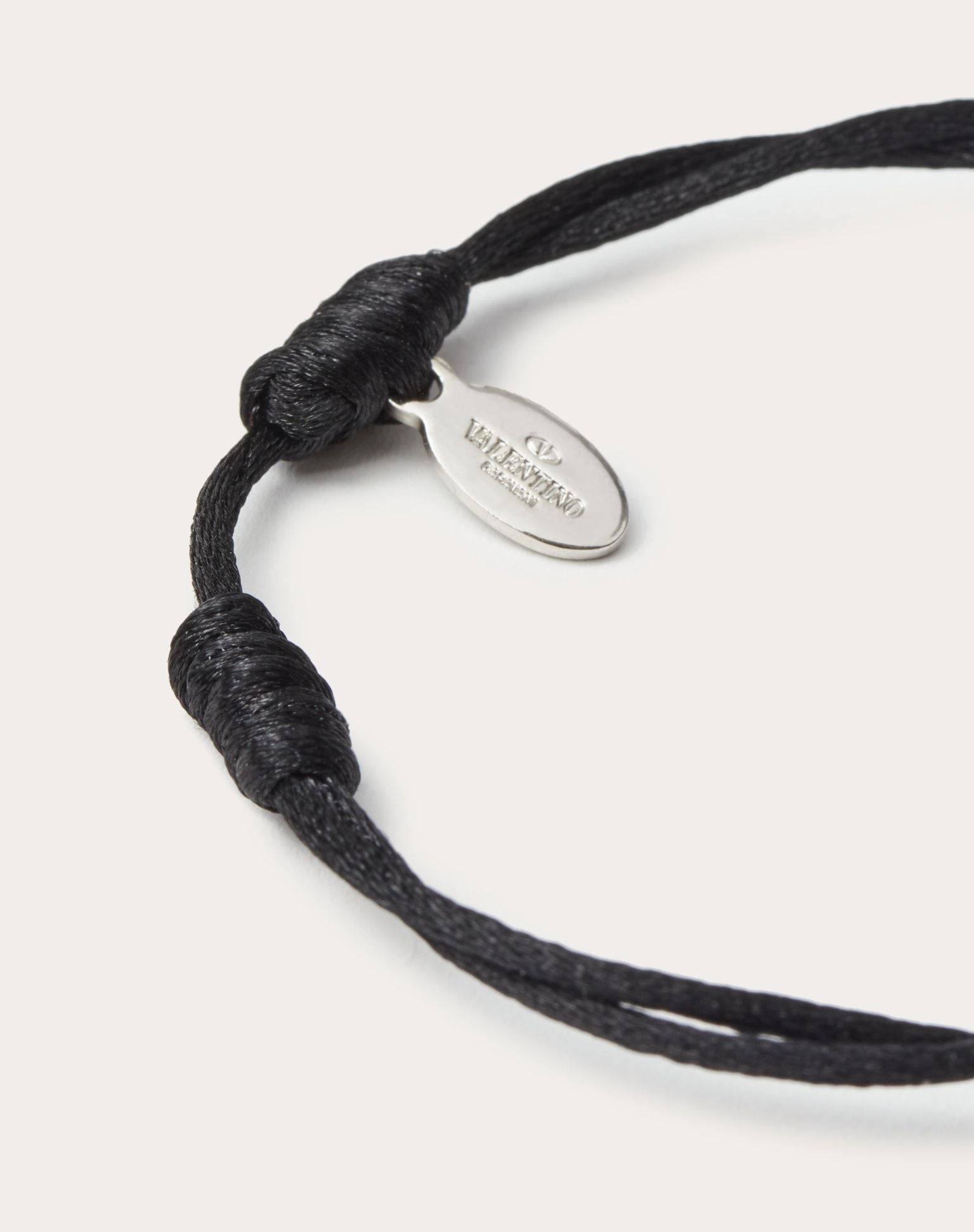 Black cord bracelet with a silver tag on a white background