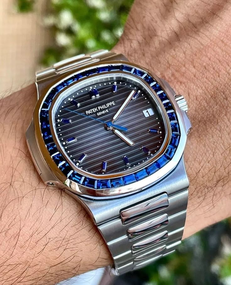 Silver watch with blue accents on a wrist against a blurred natural background