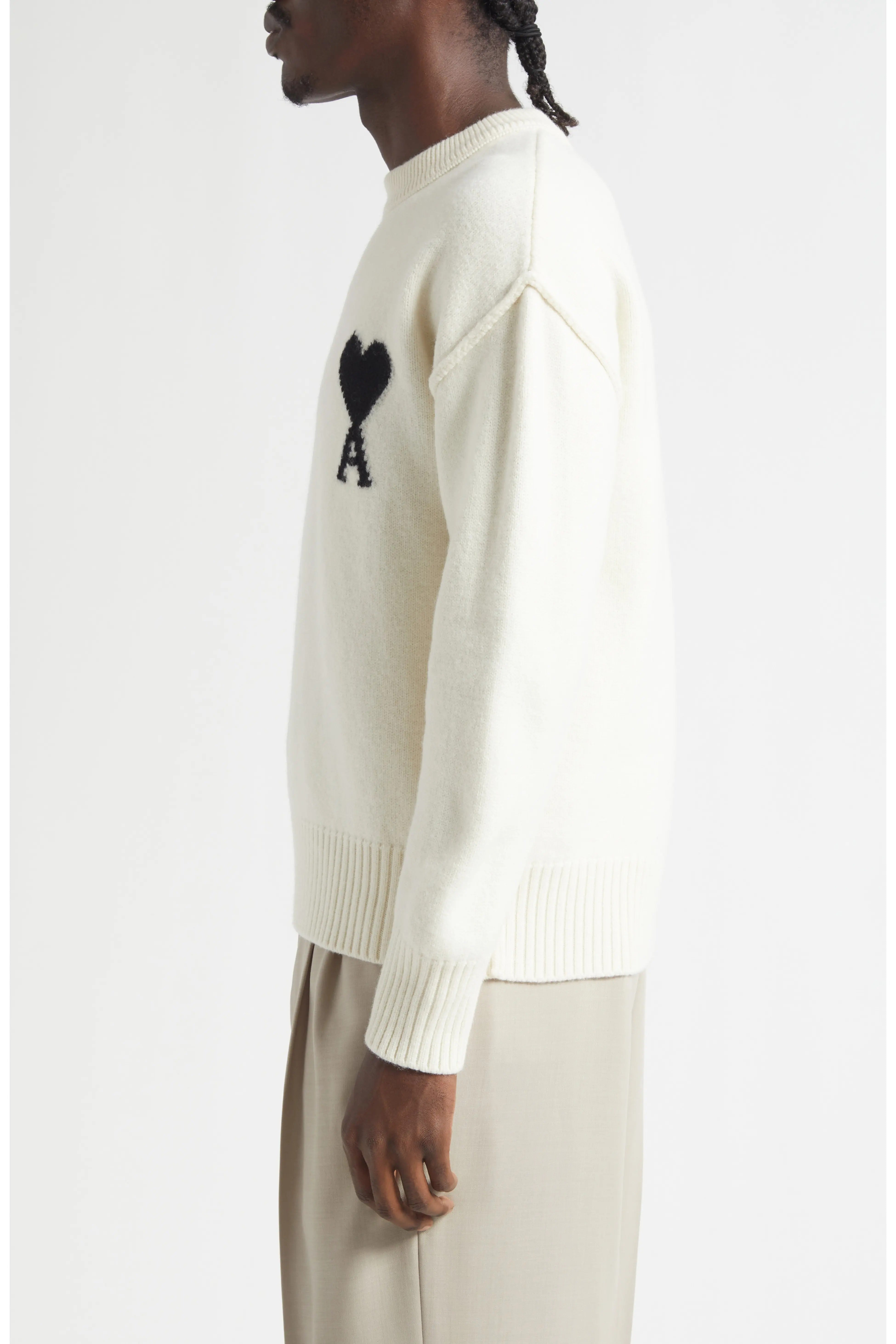Person wearing a cream sweater with a black heart and letter 'A' design on a white background