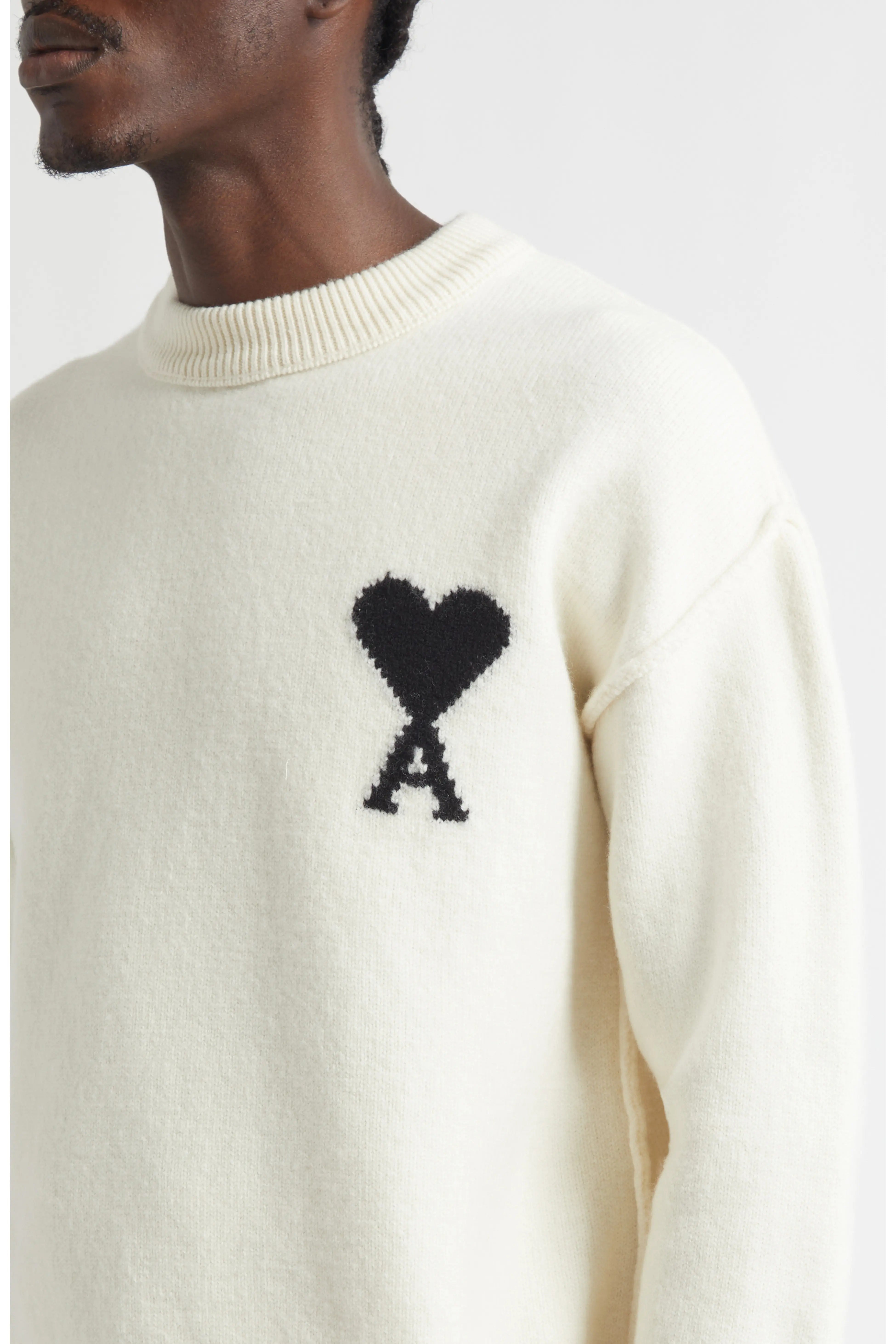 White sweater with black heart and 'A' design on a neutral background